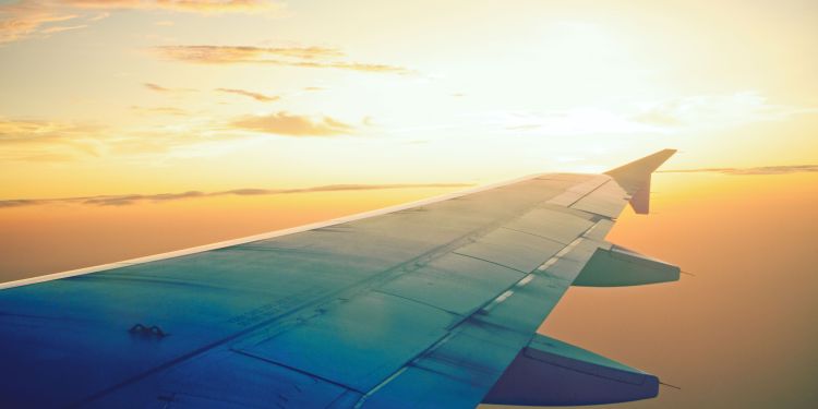 the wing of a plane as it flies through a sunset